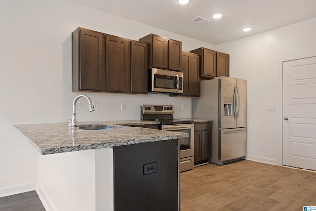 kitchen featuring sink, light wood-type flooring, appliances with stainless steel finishes, kitchen peninsula, and light stone countertops