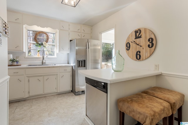 kitchen featuring a kitchen bar, sink, white cabinetry, appliances with stainless steel finishes, and backsplash