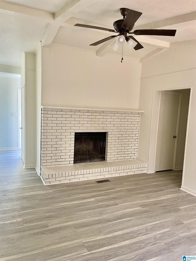 unfurnished living room with a fireplace, vaulted ceiling with beams, ceiling fan, a textured ceiling, and light hardwood / wood-style flooring