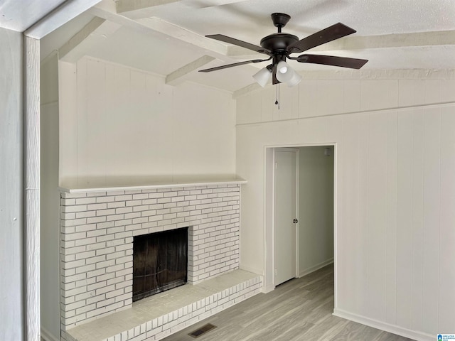 unfurnished living room featuring lofted ceiling, ceiling fan, a brick fireplace, light wood-type flooring, and wood walls