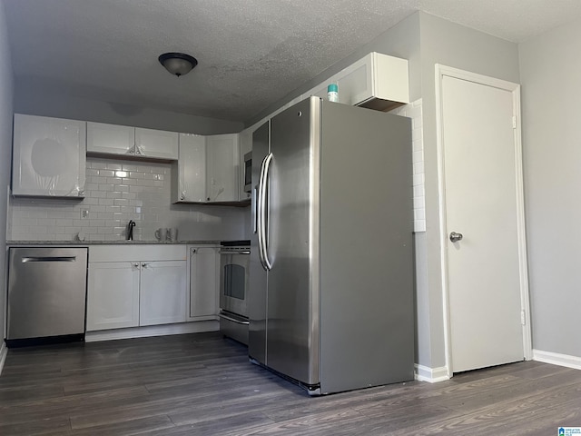 kitchen with dark wood-type flooring, a textured ceiling, appliances with stainless steel finishes, white cabinets, and backsplash