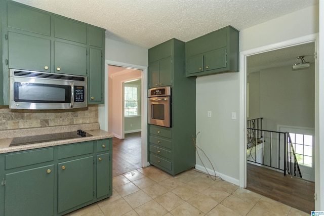 kitchen with backsplash, green cabinets, a textured ceiling, and appliances with stainless steel finishes