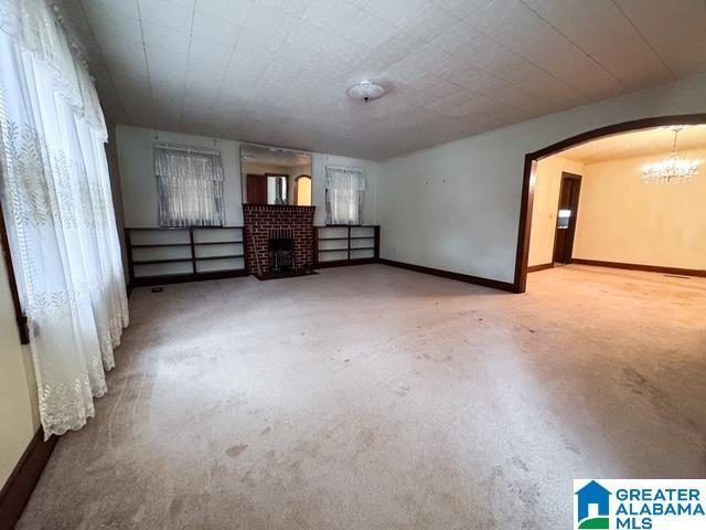 unfurnished room featuring an inviting chandelier, a brick fireplace, and carpet floors