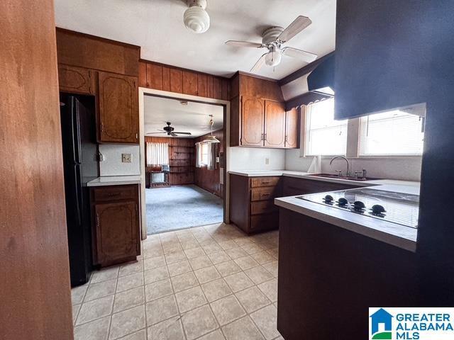 kitchen with sink, electric cooktop, black refrigerator, wooden walls, and ceiling fan