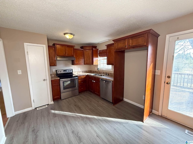 kitchen with appliances with stainless steel finishes, sink, a textured ceiling, and light wood-type flooring