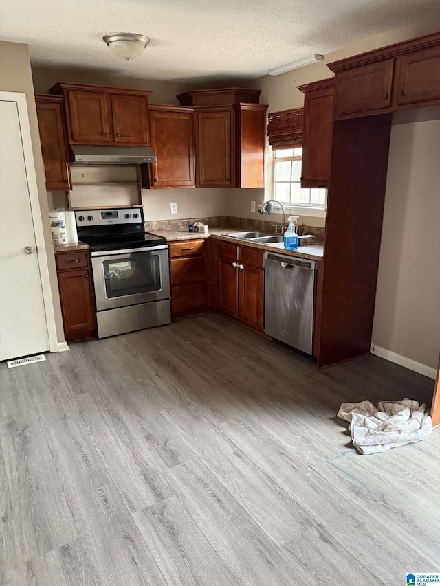 kitchen with stainless steel appliances, sink, light hardwood / wood-style flooring, and a textured ceiling