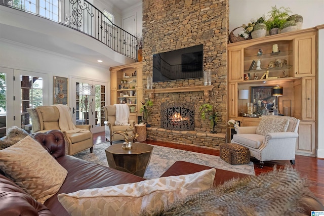 living room with built in shelves, crown molding, a fireplace, hardwood / wood-style floors, and a high ceiling