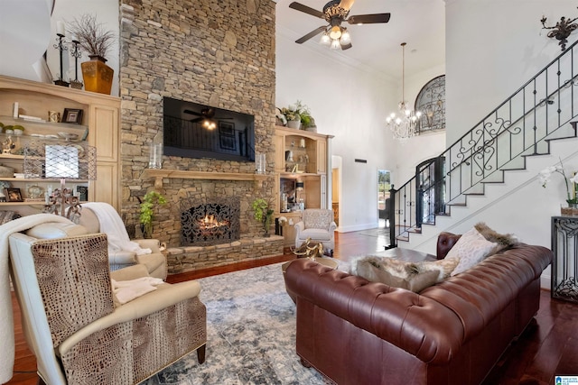 living room featuring wood-type flooring, ornamental molding, a fireplace, ceiling fan with notable chandelier, and a high ceiling