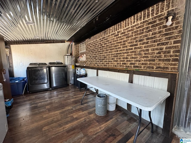 interior space featuring dark hardwood / wood-style flooring, washing machine and dryer, water heater, and brick wall