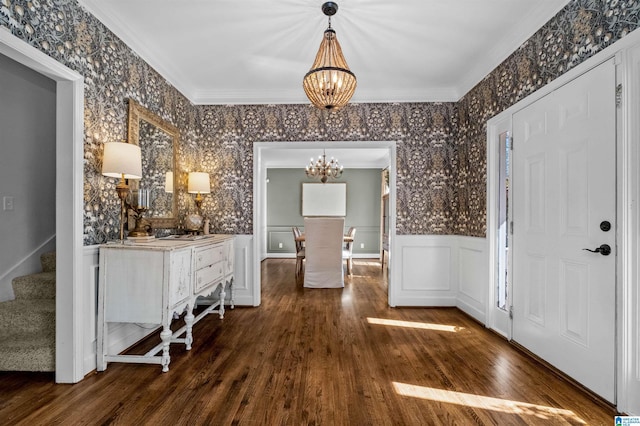 entryway with dark wood-type flooring, ornamental molding, and a chandelier