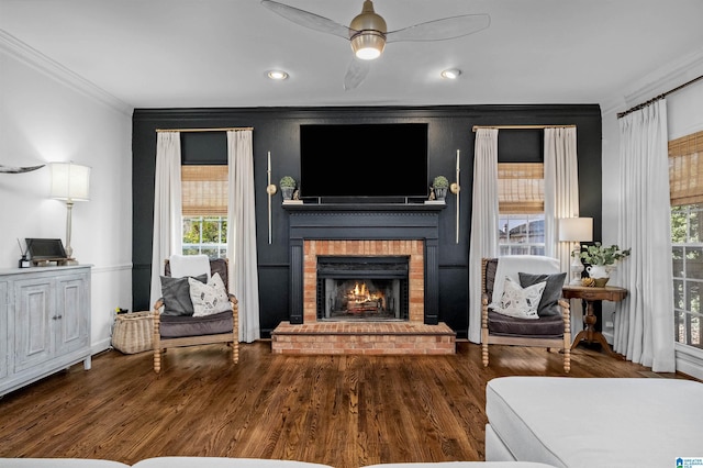 living area with crown molding, ceiling fan, wood-type flooring, and a brick fireplace