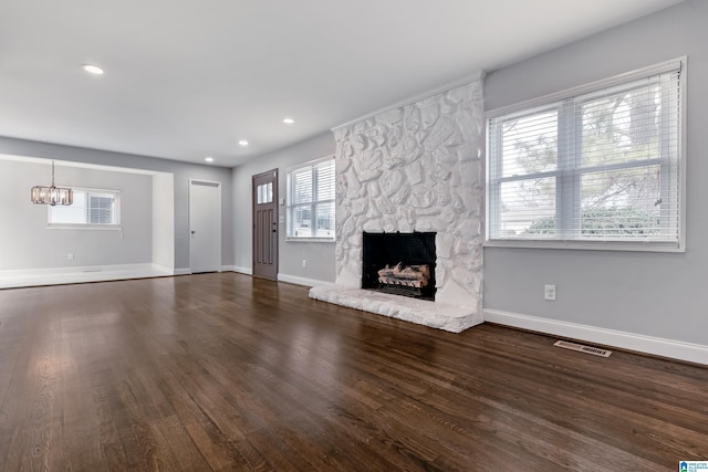 unfurnished living room featuring dark wood-type flooring, a fireplace, an inviting chandelier, and a wealth of natural light