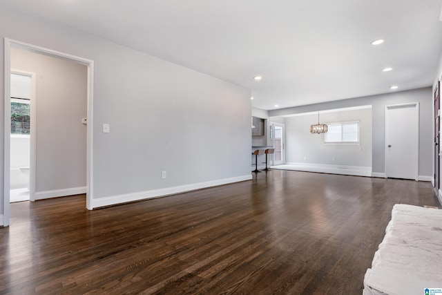 unfurnished living room featuring an inviting chandelier and dark wood-type flooring