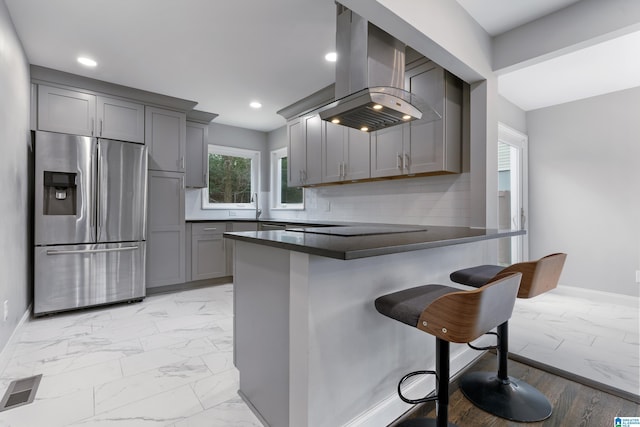 kitchen featuring gray cabinetry, stainless steel fridge with ice dispenser, kitchen peninsula, and island exhaust hood