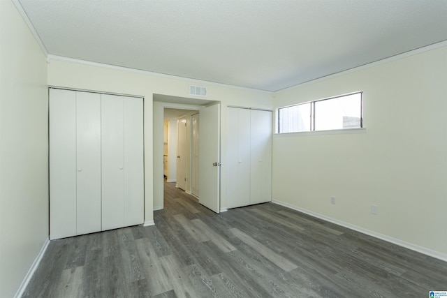 unfurnished bedroom featuring ornamental molding, dark hardwood / wood-style flooring, and two closets