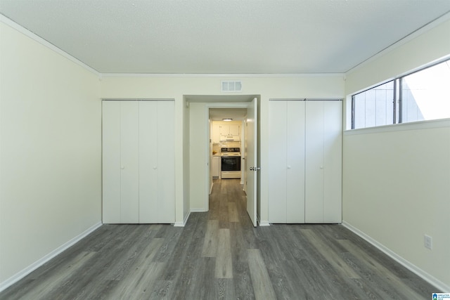 unfurnished bedroom featuring dark wood-type flooring, crown molding, and two closets