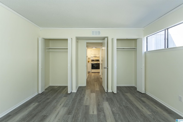 unfurnished bedroom featuring dark hardwood / wood-style flooring, crown molding, and multiple closets