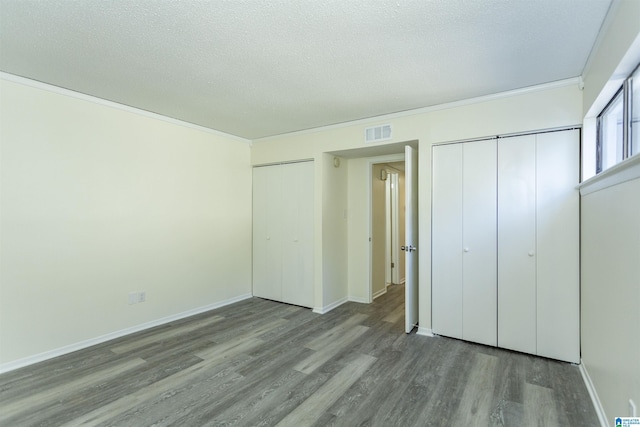 unfurnished bedroom with hardwood / wood-style floors, ornamental molding, two closets, and a textured ceiling