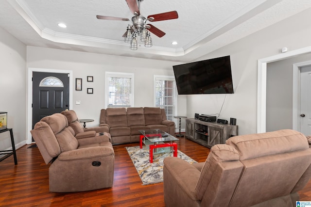 living room featuring dark wood-type flooring, a textured ceiling, ornamental molding, a tray ceiling, and ceiling fan