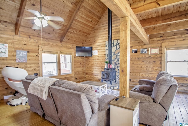 living room featuring hardwood / wood-style floors, lofted ceiling with beams, a wood stove, ceiling fan, and wooden ceiling