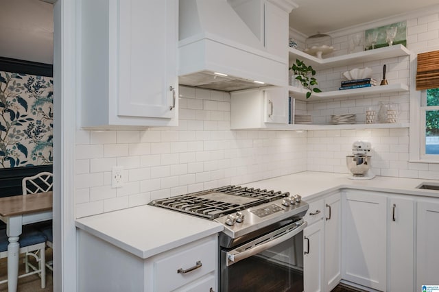 kitchen featuring premium range hood, white cabinetry, backsplash, stainless steel range with gas stovetop, and ornamental molding