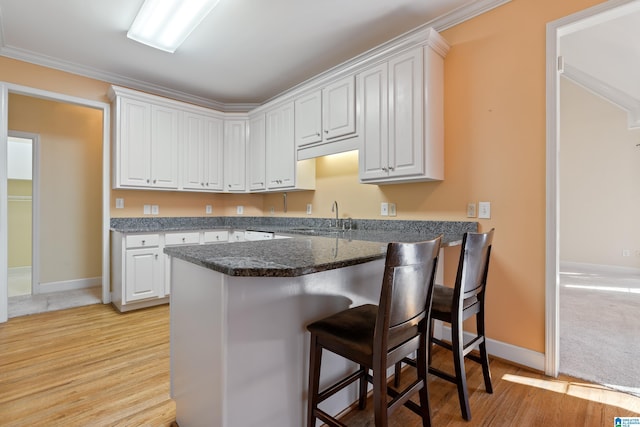 kitchen featuring sink, light hardwood / wood-style flooring, a breakfast bar, and white cabinets