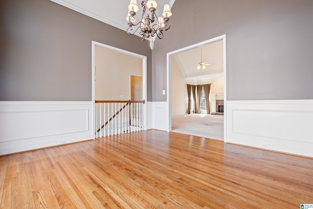 empty room featuring ceiling fan with notable chandelier, ornamental molding, and light hardwood / wood-style floors