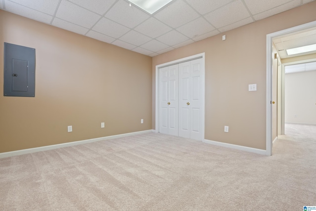 unfurnished bedroom featuring a drop ceiling, light carpet, electric panel, and a closet