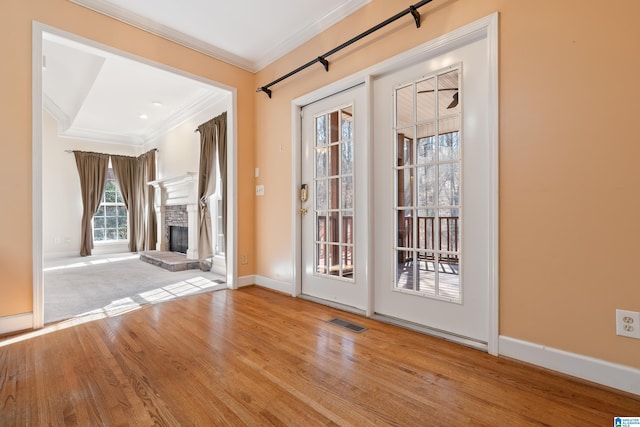 doorway to outside featuring crown molding, a stone fireplace, and light hardwood / wood-style flooring