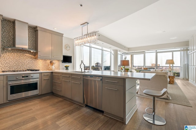 kitchen with sink, hanging light fixtures, stainless steel appliances, light hardwood / wood-style floors, and wall chimney exhaust hood