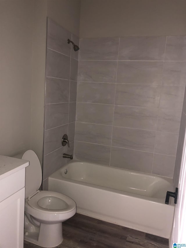 full bathroom with hardwood / wood-style flooring, vanity, tiled shower / bath combo, and toilet