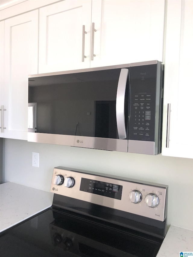 room details featuring stainless steel appliances, white cabinetry, and light stone countertops