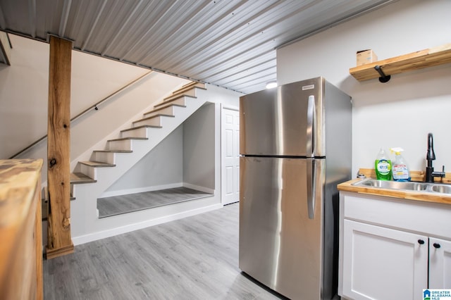 kitchen featuring white cabinetry, sink, stainless steel fridge, and light hardwood / wood-style floors