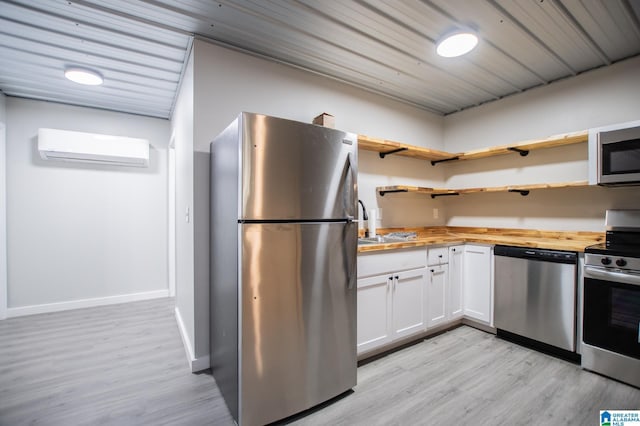 kitchen featuring wood counters, white cabinetry, a wall mounted AC, light hardwood / wood-style flooring, and appliances with stainless steel finishes