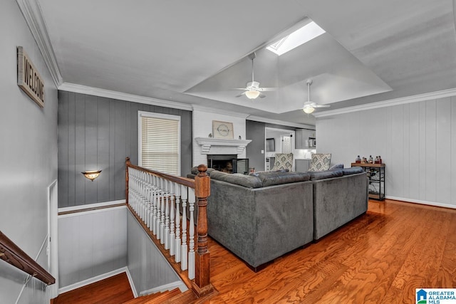 living room featuring ceiling fan, a skylight, wood-type flooring, ornamental molding, and a brick fireplace