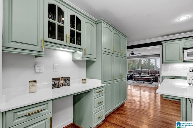 kitchen featuring crown molding, hardwood / wood-style flooring, green cabinets, white microwave, and built in desk