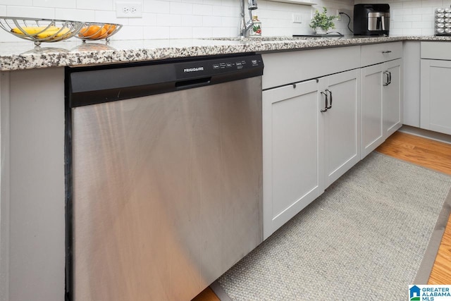 kitchen with tasteful backsplash, light stone counters, stainless steel dishwasher, and light hardwood / wood-style floors