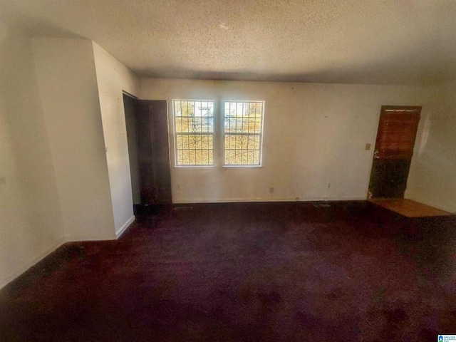 empty room with a textured ceiling and dark colored carpet