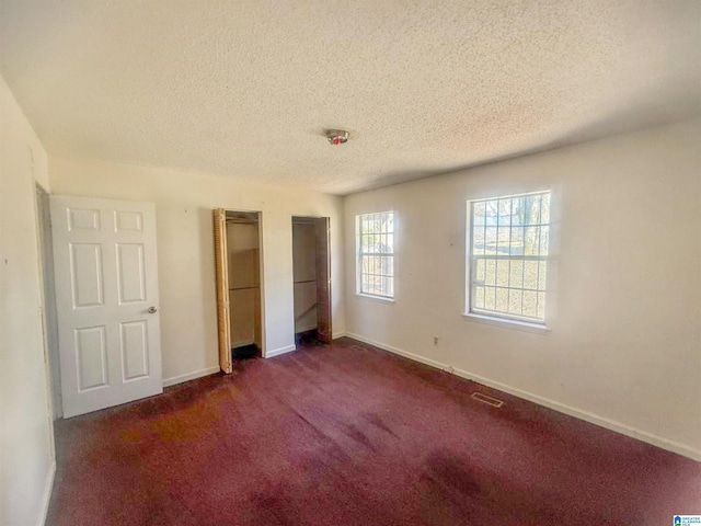 unfurnished bedroom with dark carpet, a textured ceiling, and two closets