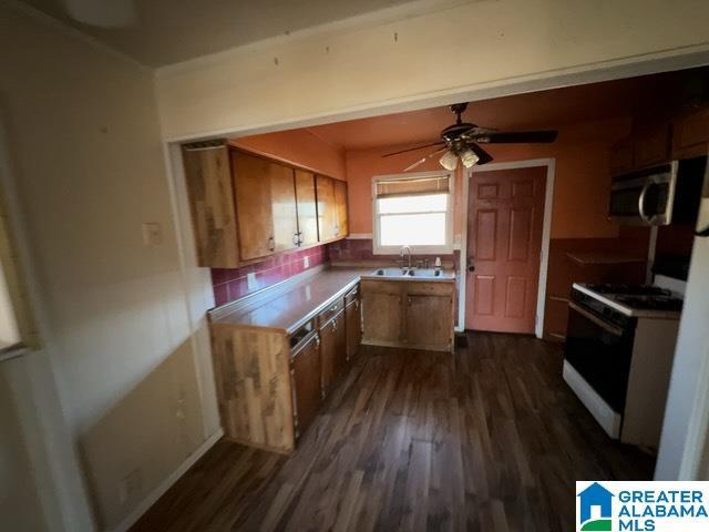 kitchen with white gas stove, stainless steel microwave, a sink, and brown cabinetry