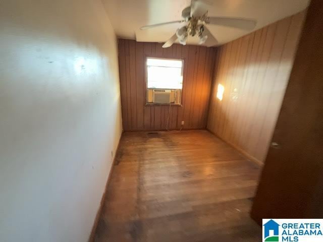 spare room featuring wood walls, a ceiling fan, cooling unit, and wood finished floors