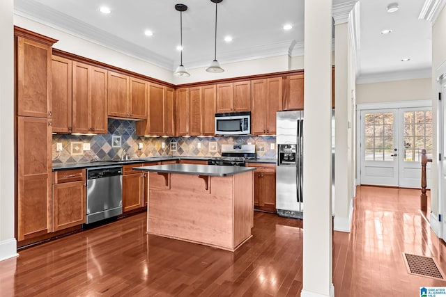 kitchen featuring appliances with stainless steel finishes, a kitchen bar, hanging light fixtures, ornamental molding, and a center island