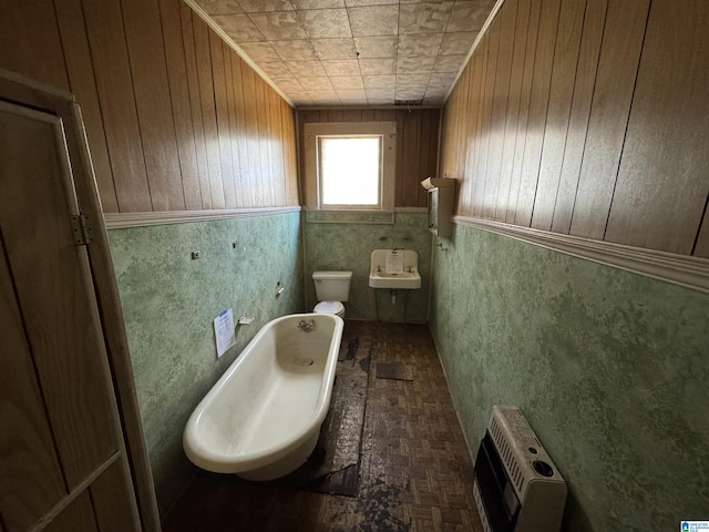 bathroom with wooden walls, toilet, a bathing tub, and heating unit