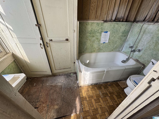 bathroom with parquet floors, a tub, and toilet