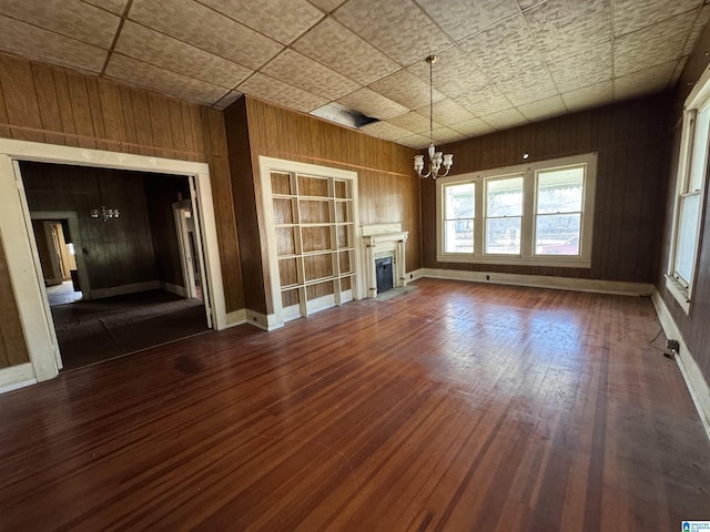 unfurnished living room featuring dark wood-type flooring, an inviting chandelier, and wood walls