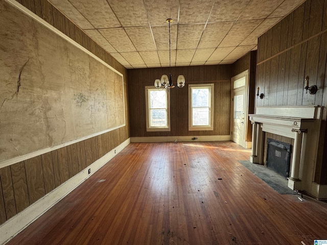 unfurnished living room featuring a notable chandelier, a tiled fireplace, hardwood / wood-style floors, and wood walls