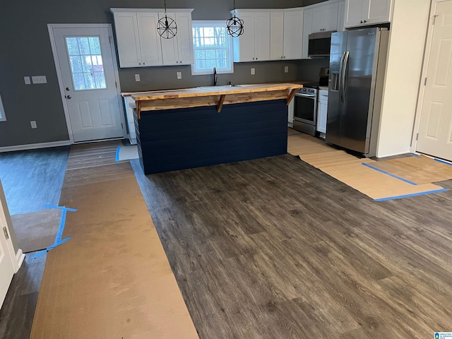 kitchen with appliances with stainless steel finishes, butcher block countertops, decorative light fixtures, white cabinetry, and sink