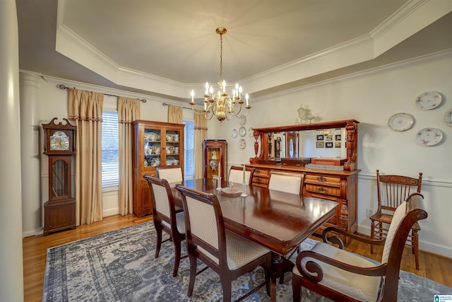 dining space with ornamental molding, a tray ceiling, hardwood / wood-style floors, and a notable chandelier