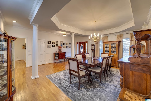 dining room with decorative columns, a raised ceiling, a notable chandelier, and light hardwood / wood-style floors