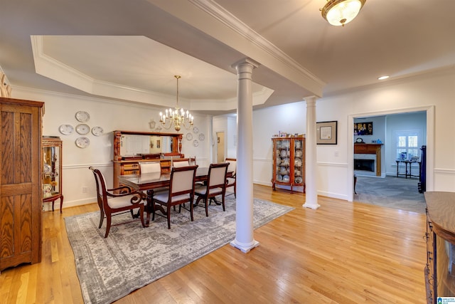 dining space featuring a tray ceiling, light hardwood / wood-style flooring, ornamental molding, and ornate columns